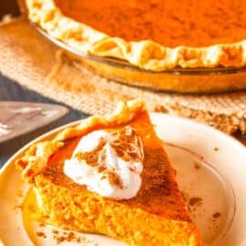 Slice of healthy pumpkin pie cut, topped with whipped cream, and served on a white plate, side view.