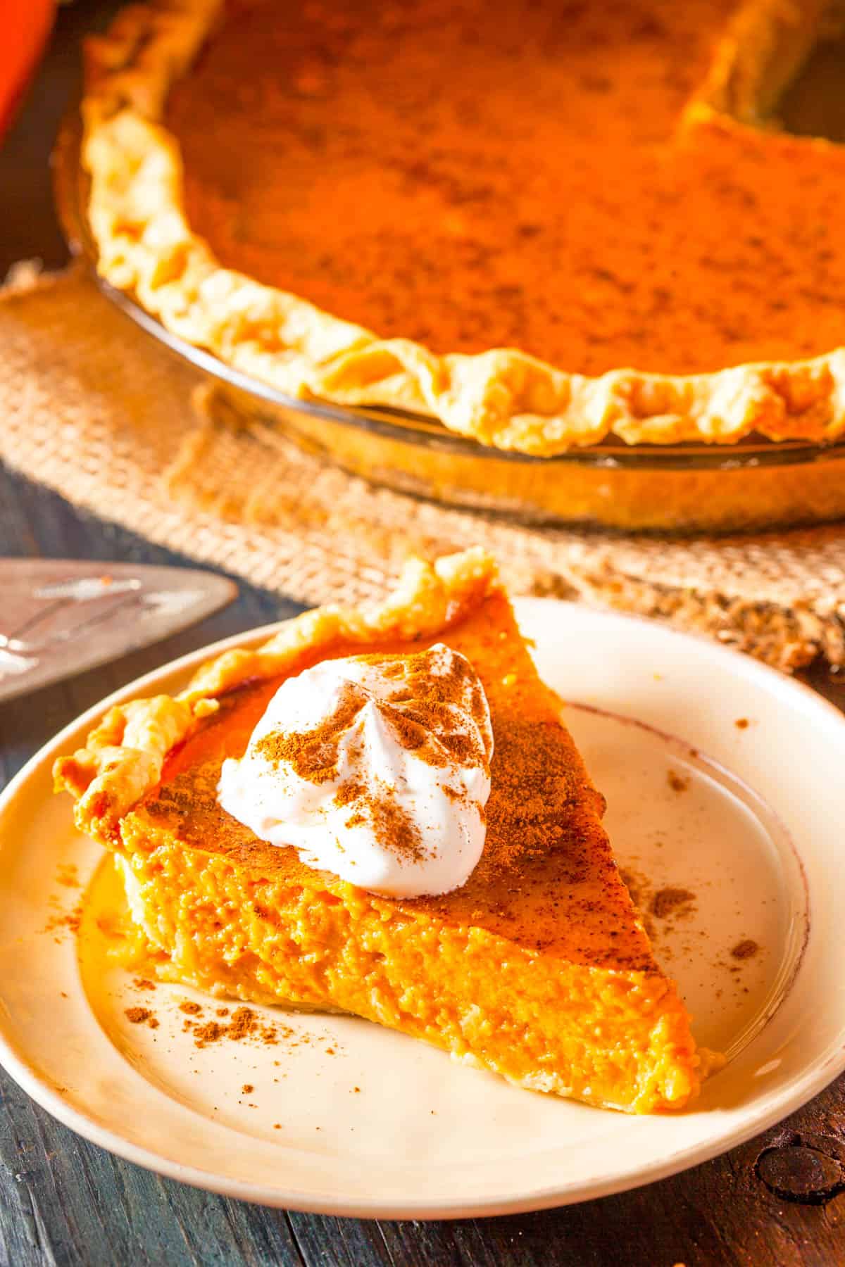 Slice of healthy pumpkin pie cut, topped with whipped cream, and served on a white plate, side view.