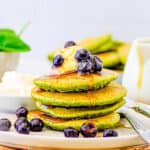 Healthy spinach pancakes for kids, toddlers, or even adults stacked on a white plate, topped with berries and maple syrup.