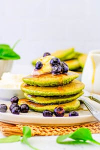 Healthy spinach pancakes for kids, toddlers, or even adults stacked on a white plate, topped with berries and maple syrup.
