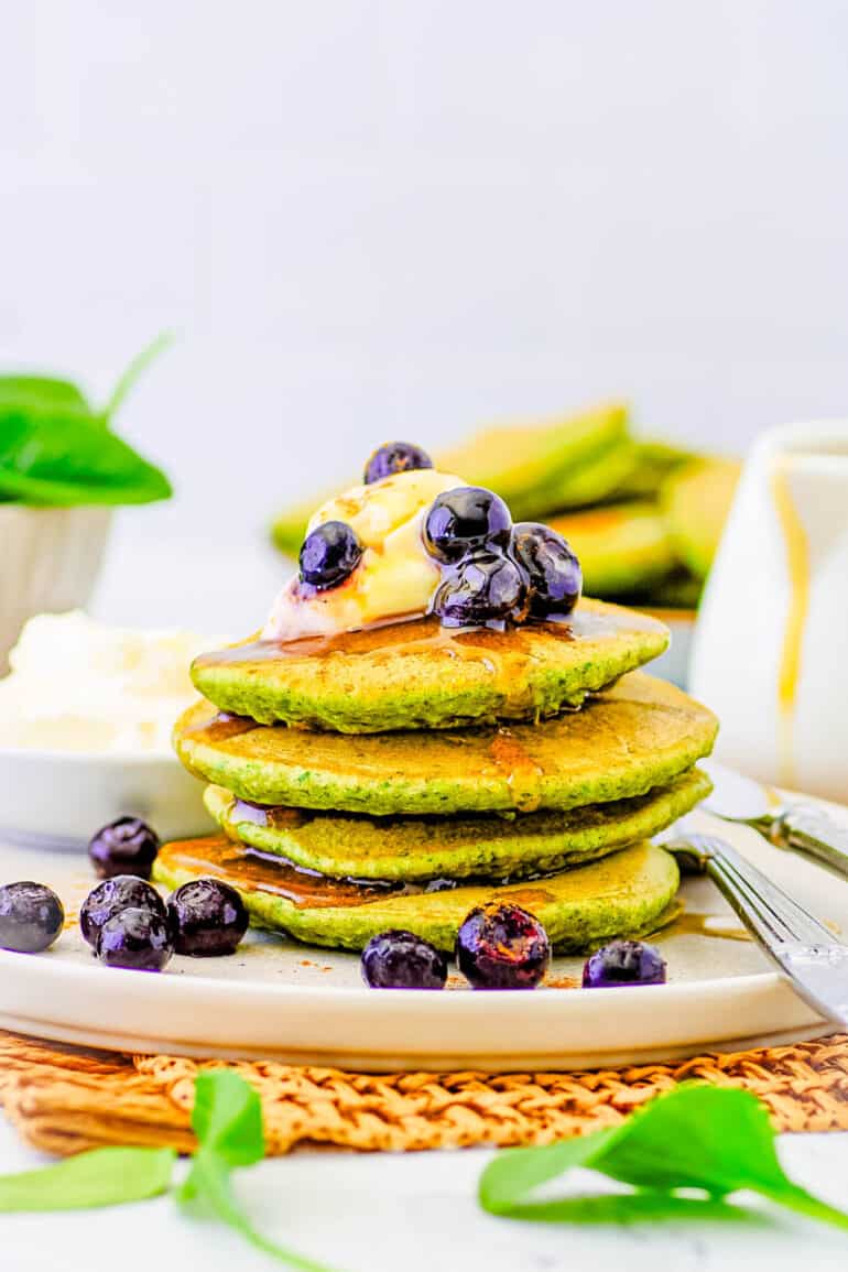 Healthy spinach pancakes for kids, toddlers, or even adults stacked on a white plate, topped with berries and maple syrup.