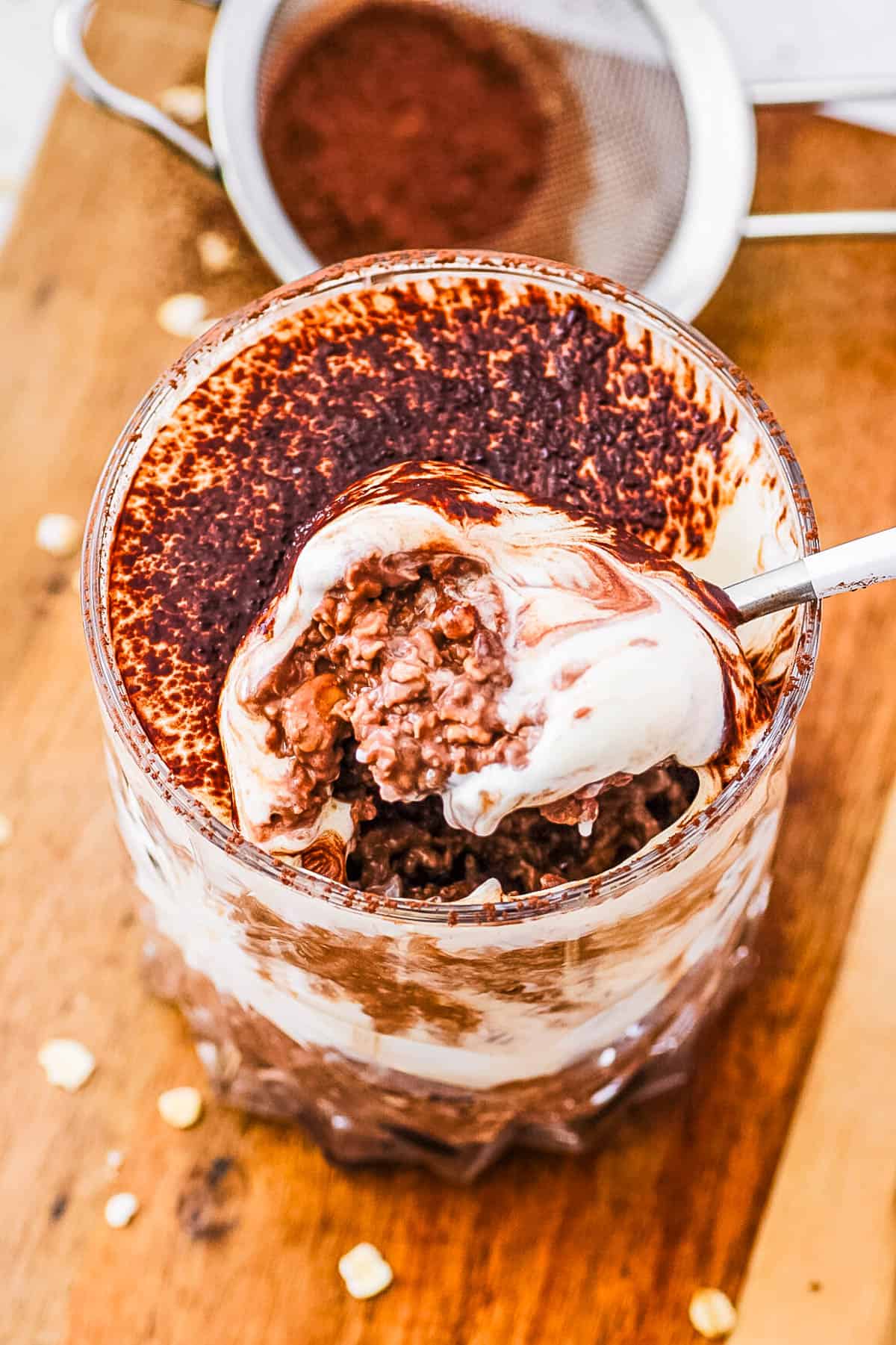 Healthy tiramisu overnight oats in a glass, with a spoonful being taken out of the top.