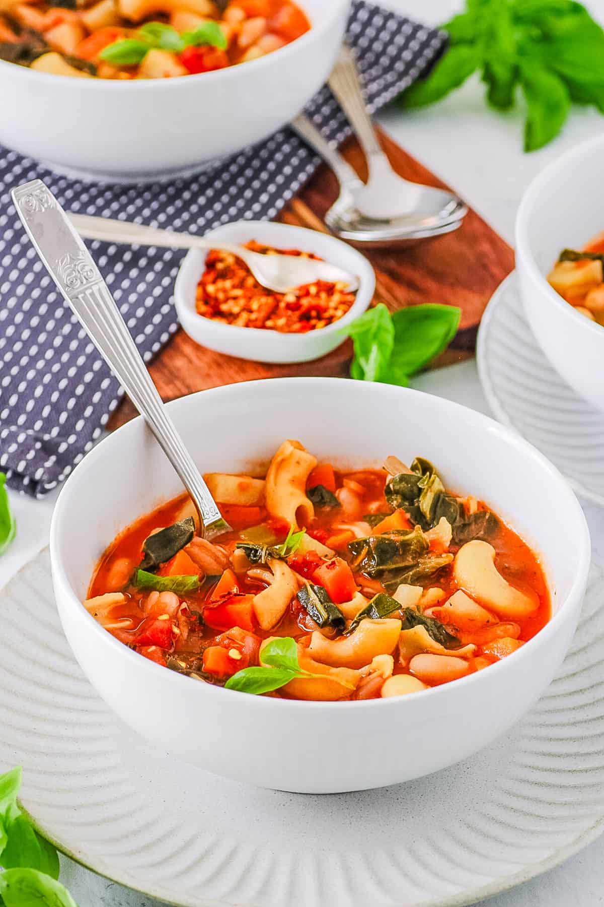 Healthy vegan minestrone soup served in a white bowl with a spoon.