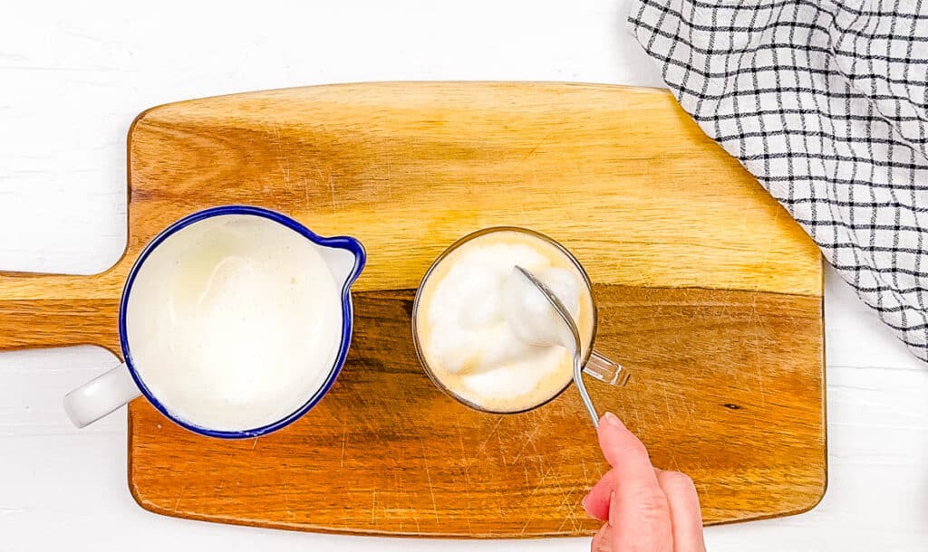 Frothed oat milk being added to honey bee latte in a glass.