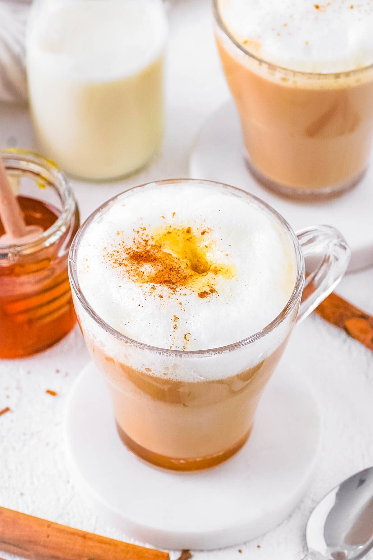 Honey latte served in a glass coffee mug on a white plate.