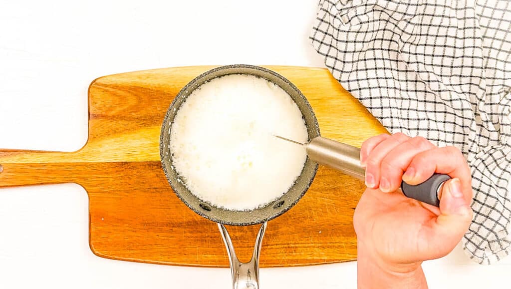 Oatmilk being frothed in a small pot with a milk frother.