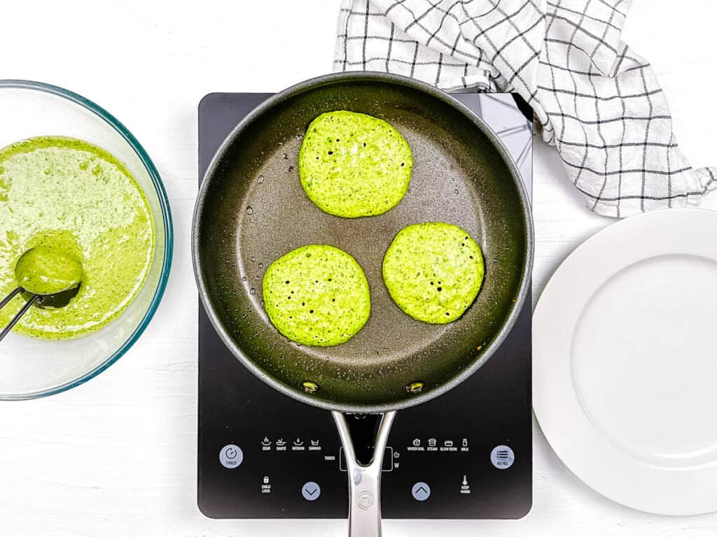 Spinach blender pancakes cooking in a pan on the stove.