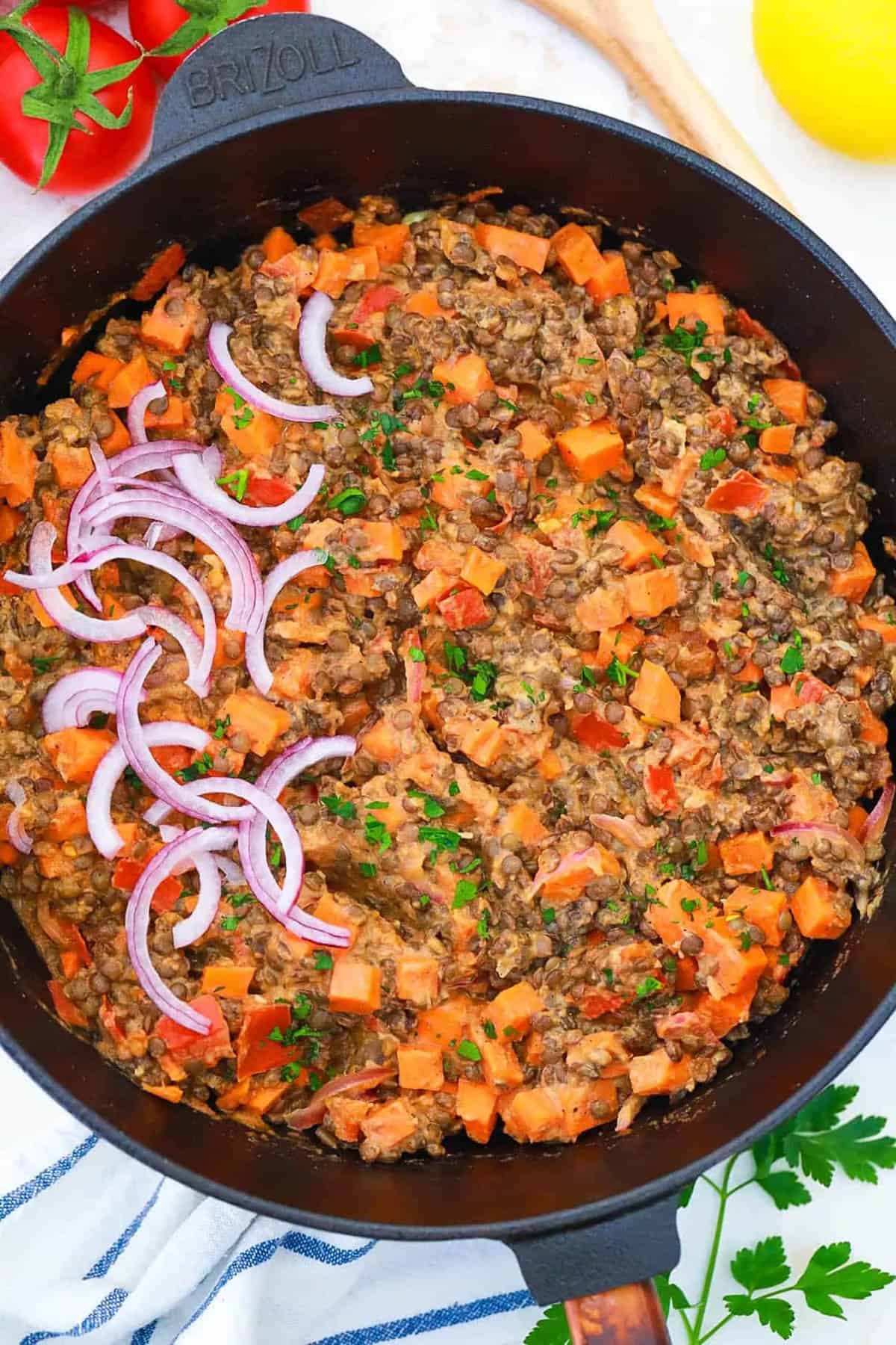 Vegan dinner recipe for lentils and tahini served in a cast iron skillet, garnished with red onions.