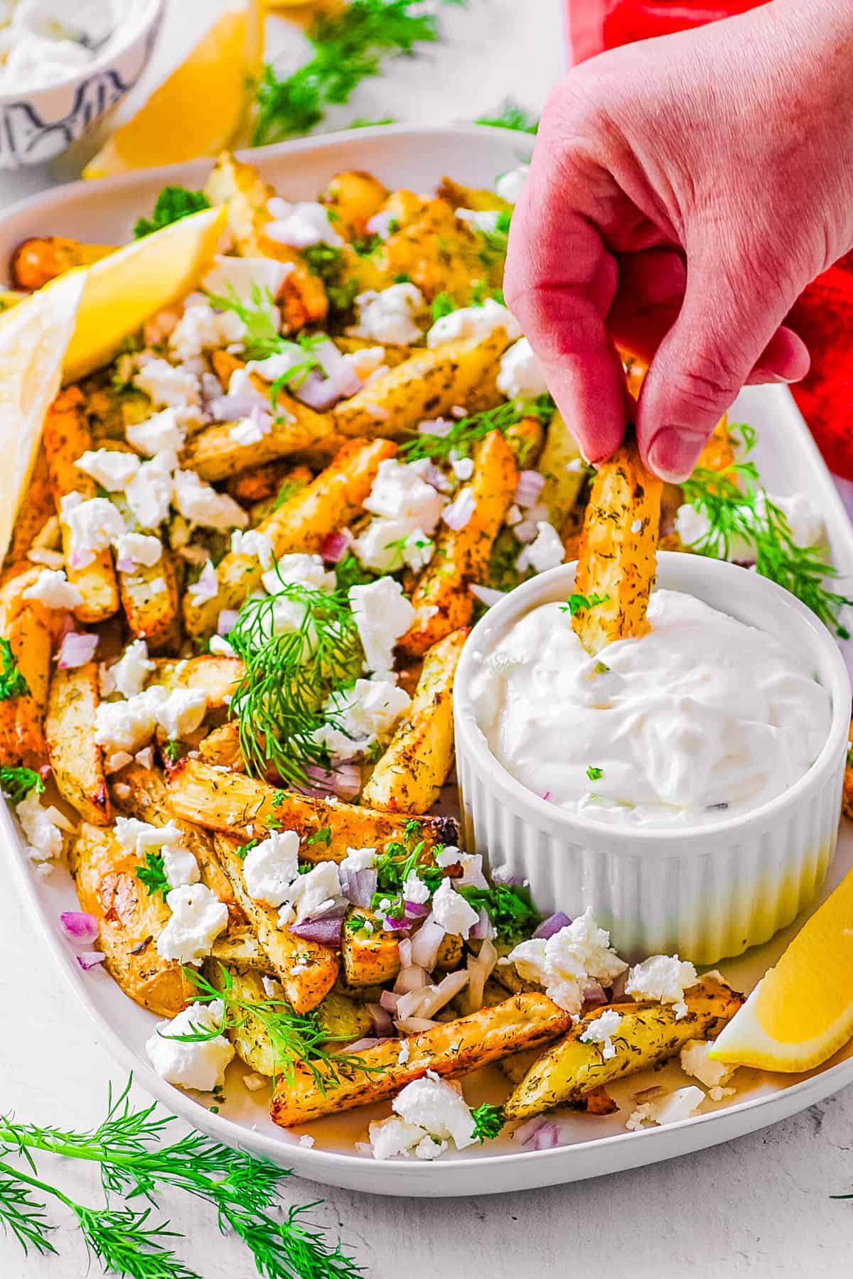 Loaded Greek fries with feta, parsley, onions, and tzatziki dip on the side, served on a white plate.