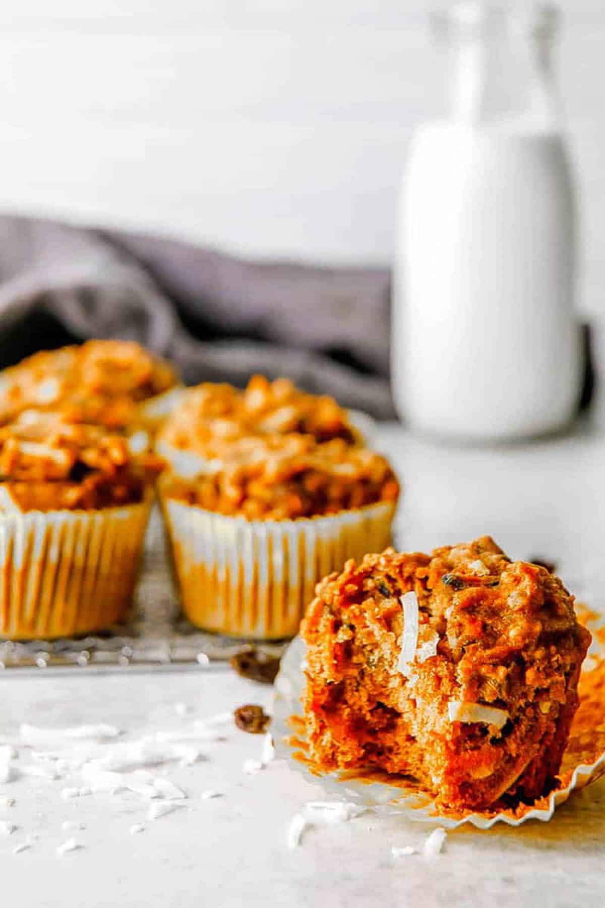Healthy apple carrot muffins on the counter with shredded coconut and a jar of milk in the background.