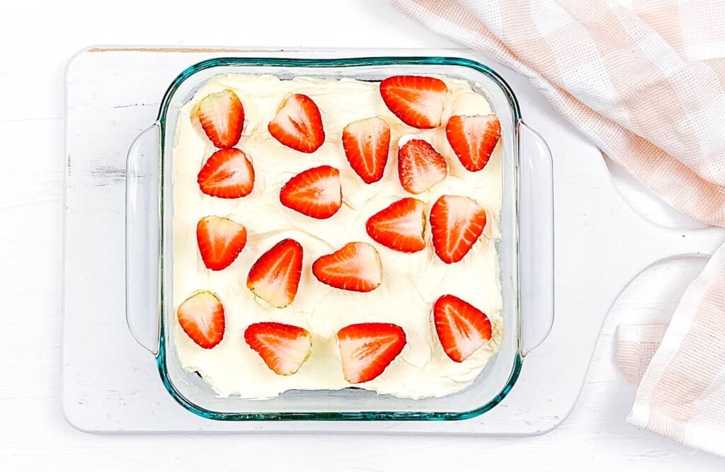 Low calorie gf tres leches cake topped with whipped cream and strawberries in a baking dish.
