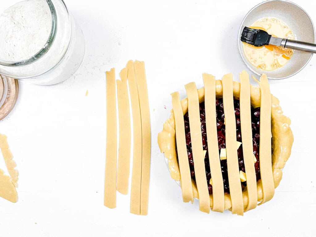 Pie crust being assembled into a lattice design on top of the cherry pie.