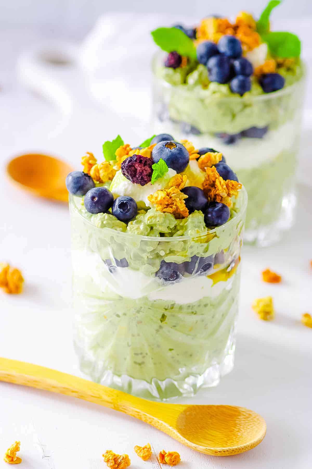 Light green matcha overnight oats in a clear glass cup, layered with yogurt and topped with blueberries, granola, and mint.