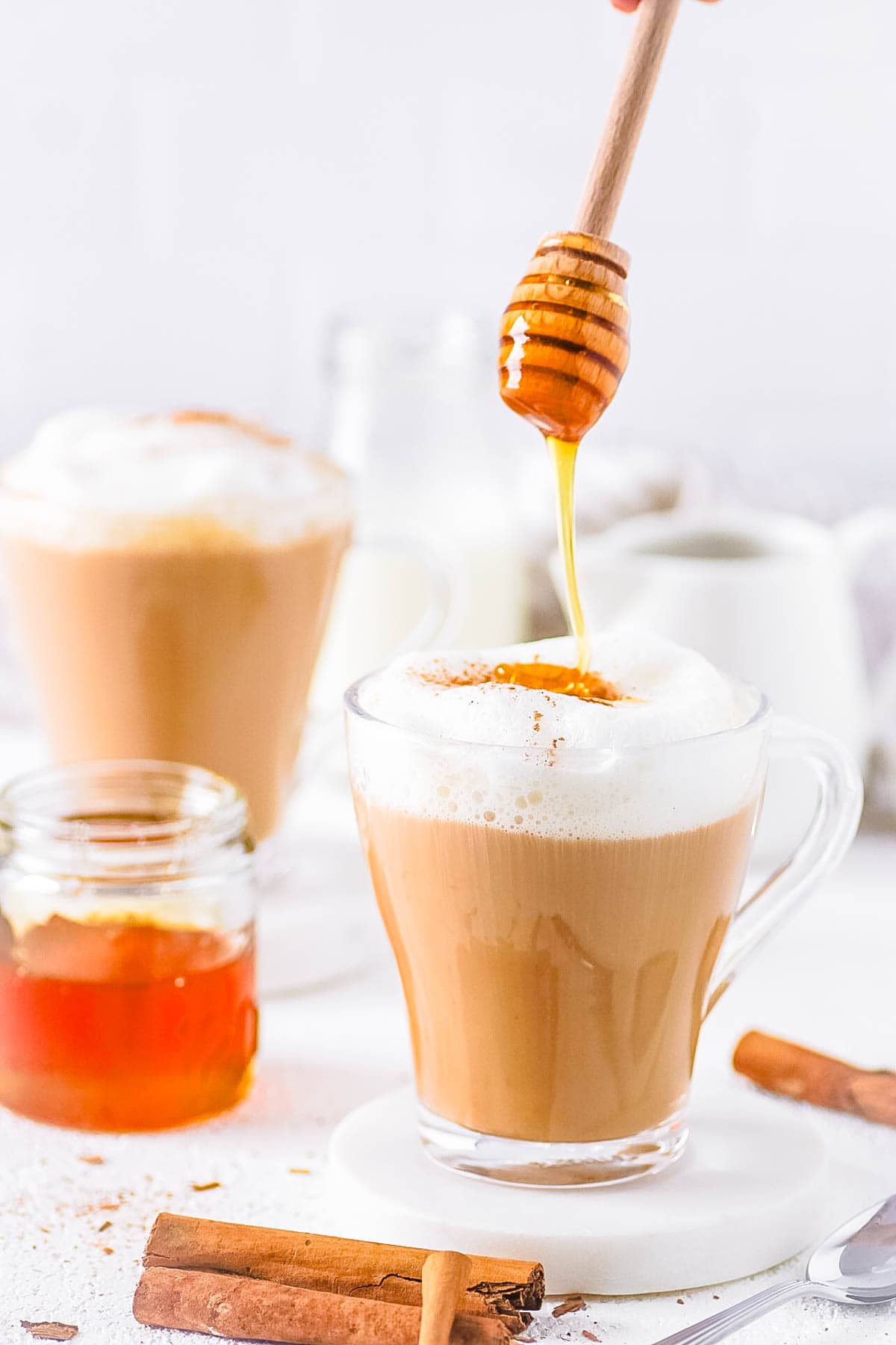 Oatmilk honey latte, served in a glass coffee mug with honey being drizzled on top.