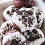 Baked Oreo donuts with a cream cheese frosting, stacked on a white serving plate.