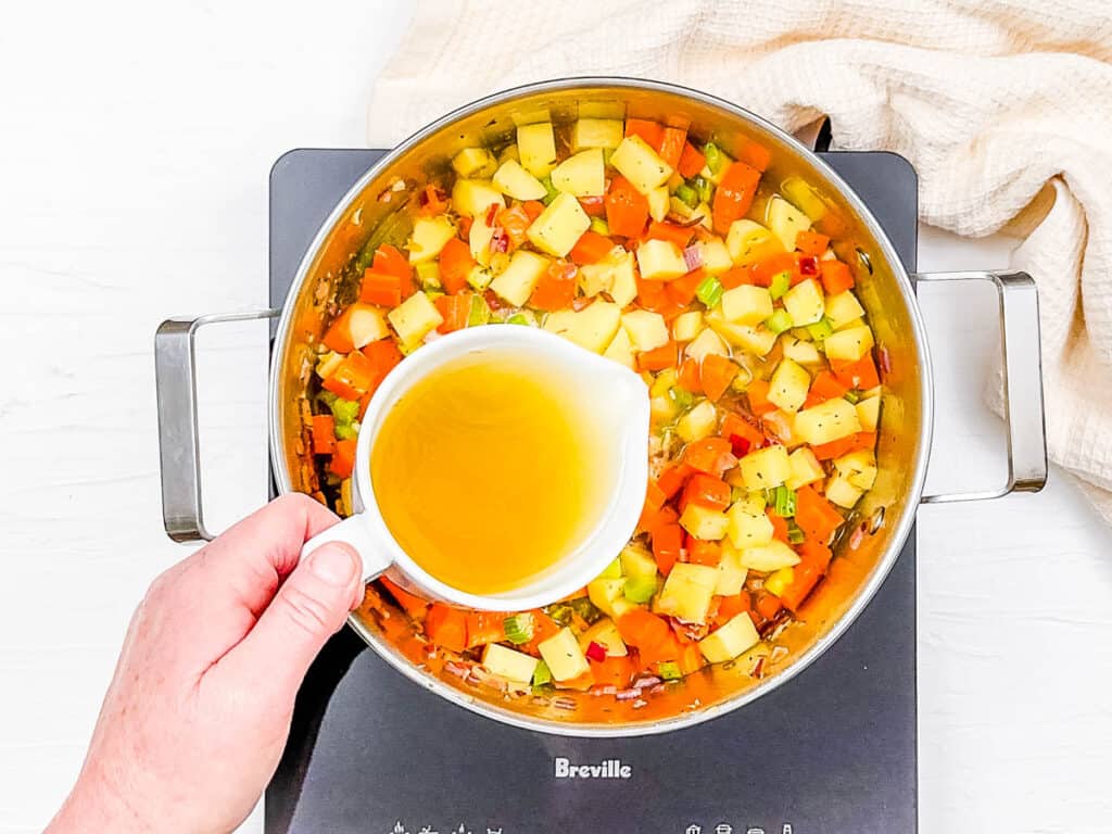 Broth added to sauteed veggies in a pot on the stove.