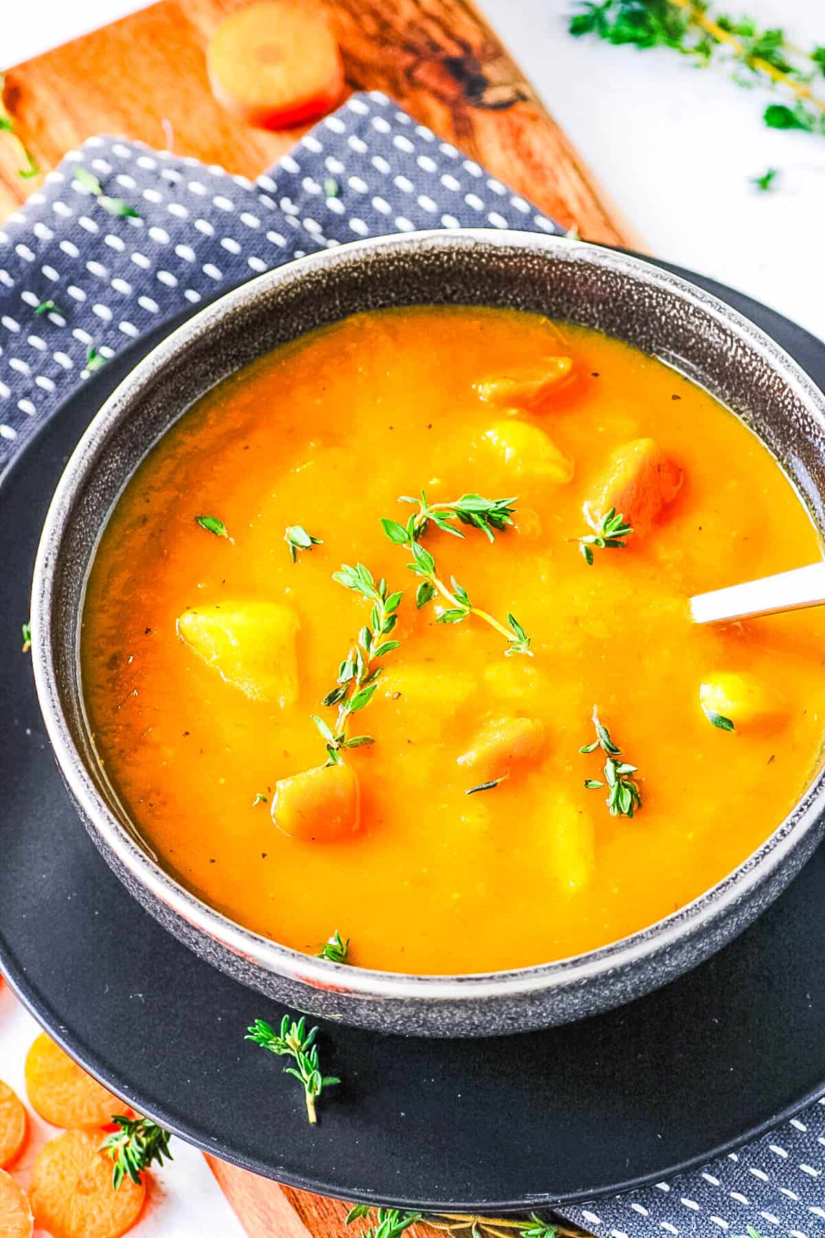 Healthy carrot potato soup, served in a dark grey bowl, garnished with fresh herbs.