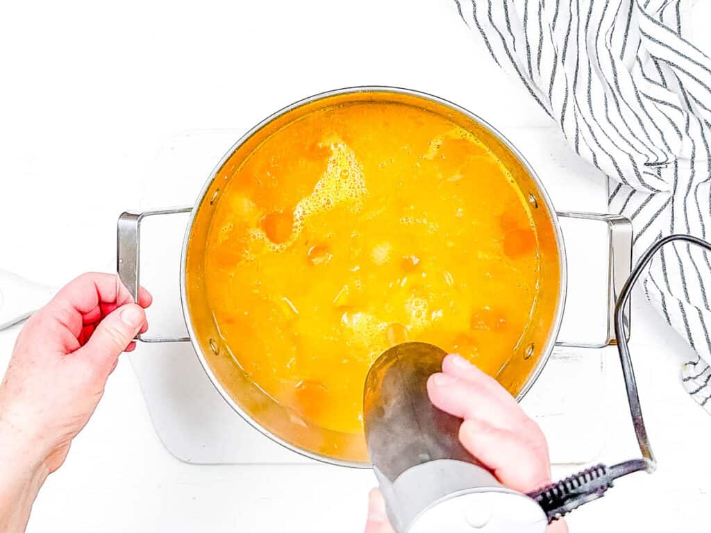 Immersion blender blending butternut squash, carrots and veggies into a pureed soup.