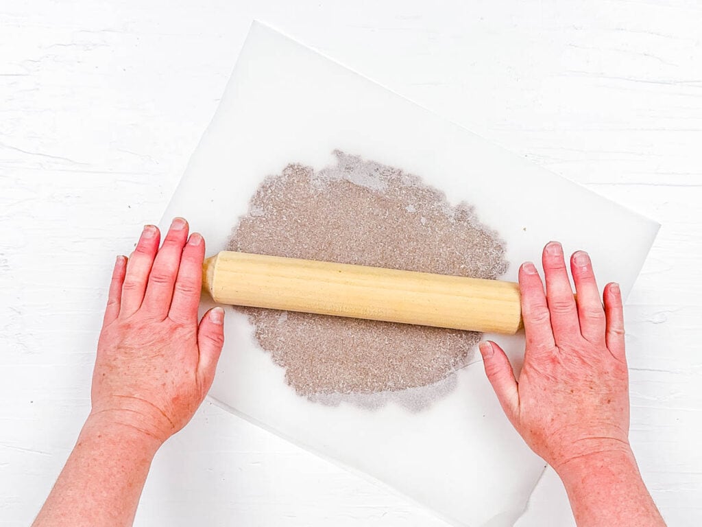 Cereal dough being rolled out between two sheets of parchment paper.