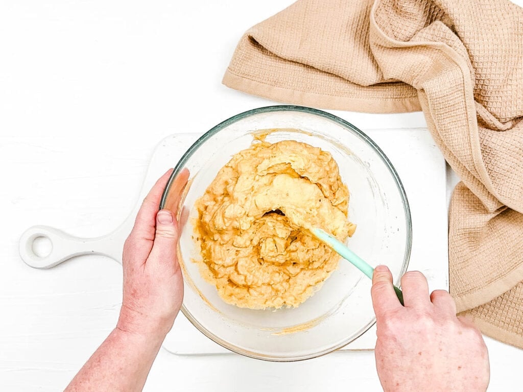 Sour cream added to mashed potatoes and spices, mixed in a bowl.