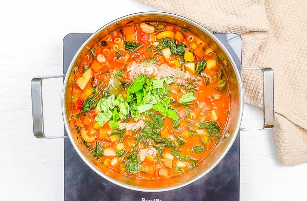 Vegetarian minestrone soup simmering in a pot on the stove.