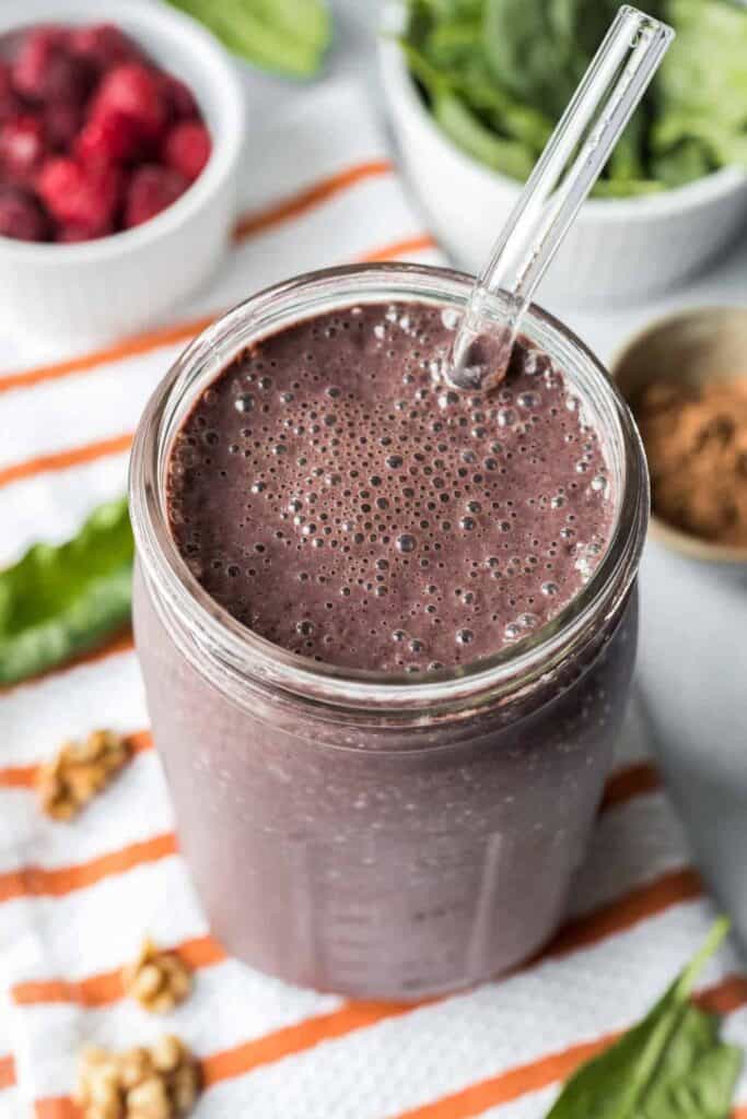 Dark purple smoothie in a clear glass jar with a clear straw.