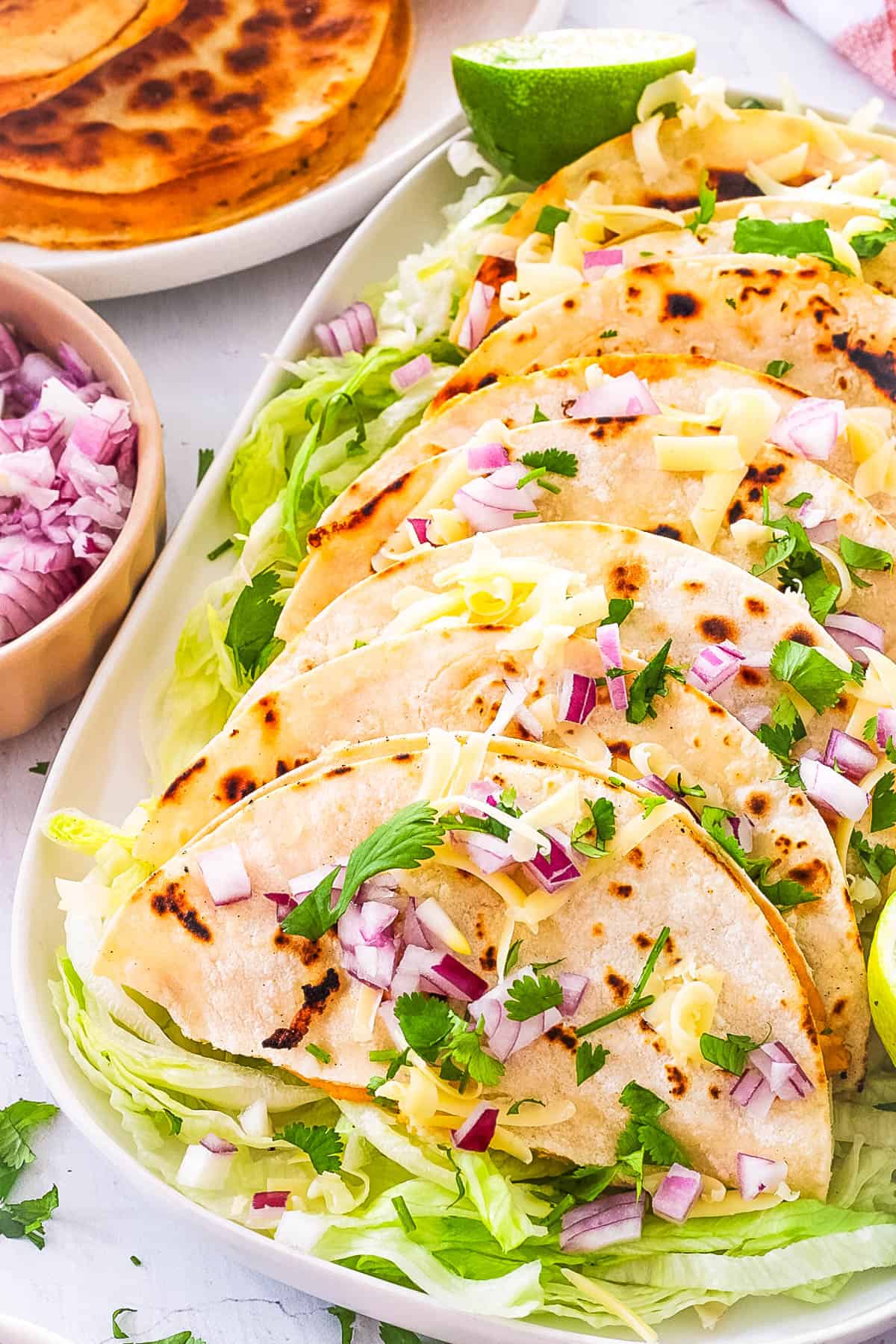 Mexican crispy potato tacos (or tacos de papas) served on a white serving plate, topped with onions and cilantro.