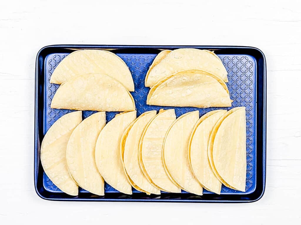 Potato tacos lined up on a baking sheet, ready to be cooked.