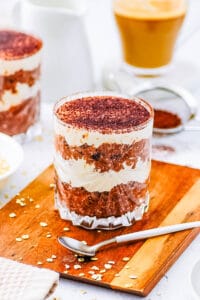 Tiramisu overnight oats, served in a glass with a spoon on the side.