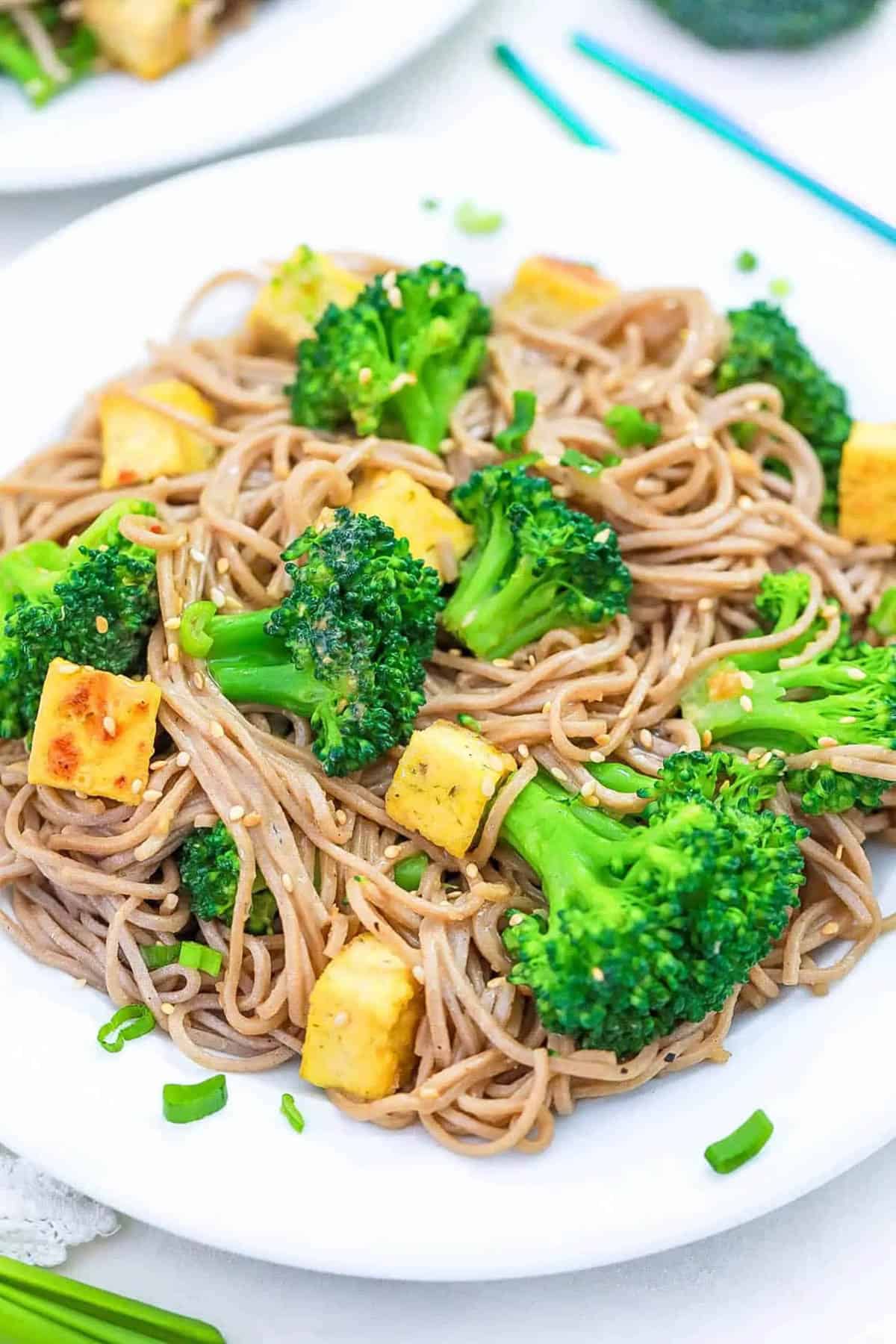 Tofu broccoli stir fry with sesame noodles served on a white plate.