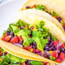 Vegan black bean tacos with beans, avocado, veggies, and cilantro, served on a white plate.