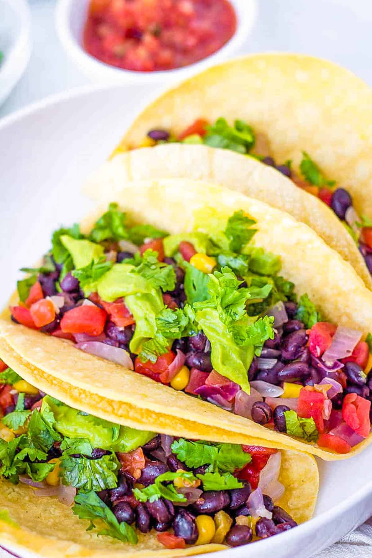 Vegan black bean tacos with beans, avocado, veggies, and cilantro, served on a white plate.