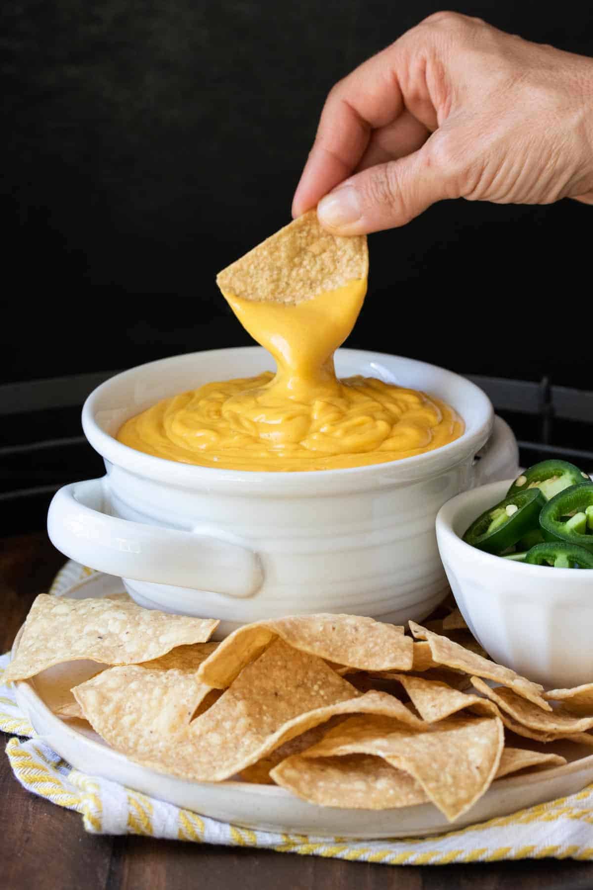 Hand dipping a chip in a bowl of orange cheese sauce.