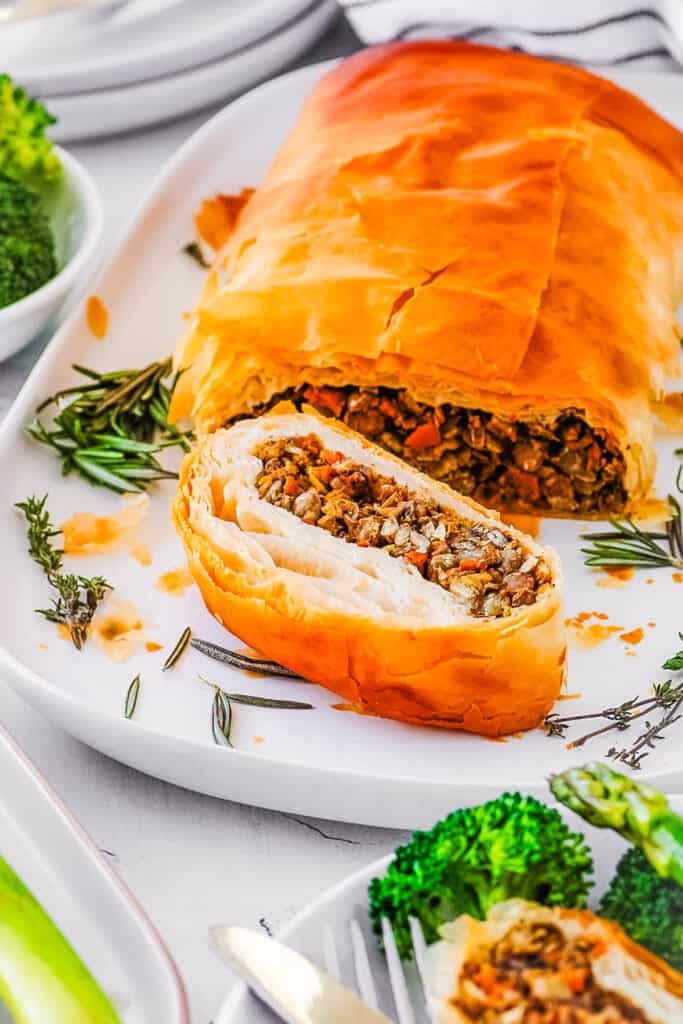 Vegan Wellington with lentils and mushrooms, served on a white plate with roasted veggies on the side.