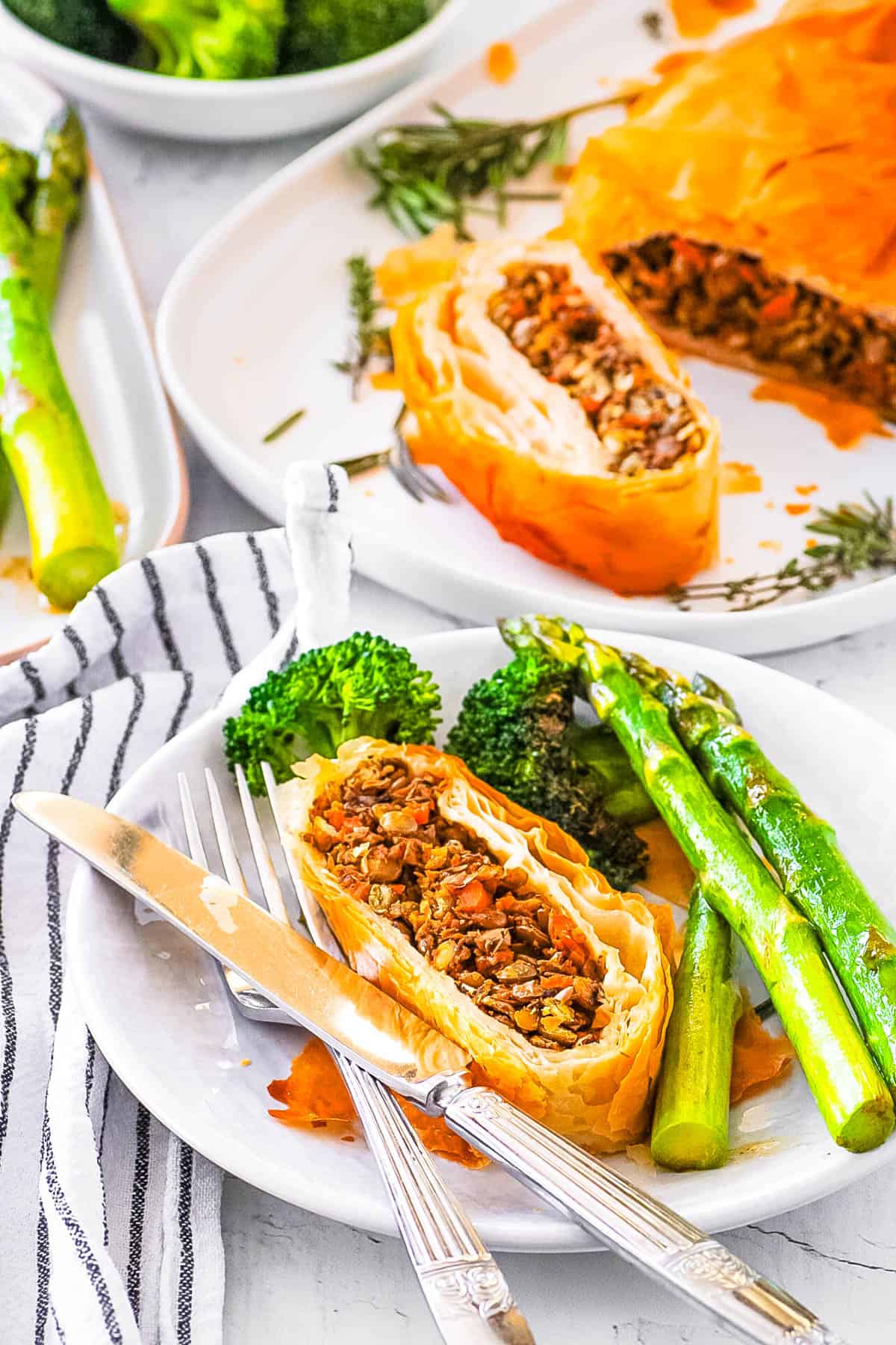 Easy vegan Wellington with lentils and mushrooms, served on a white plate with roasted veggies on the side.