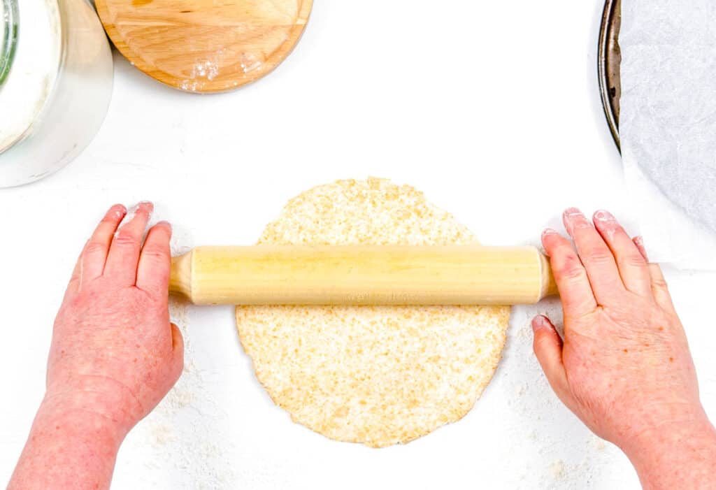 Pizza dough being rolled out on a countertop with a rolling pin.
