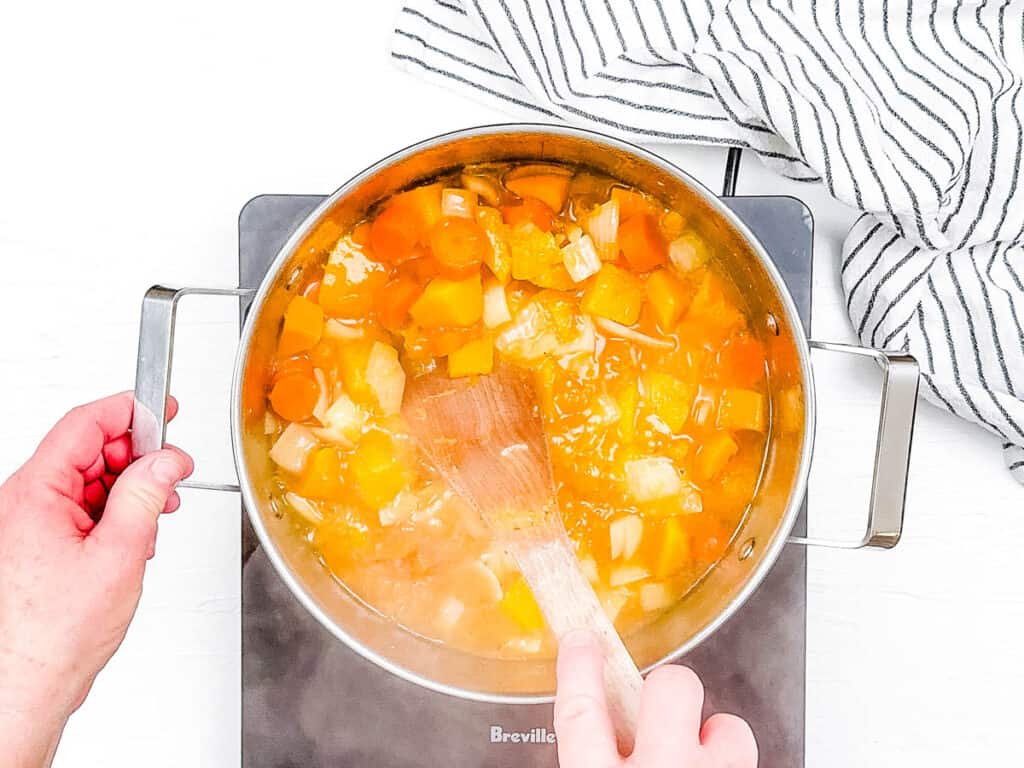 Carrots, squash and onions and broth cooking in a ، on the stove.