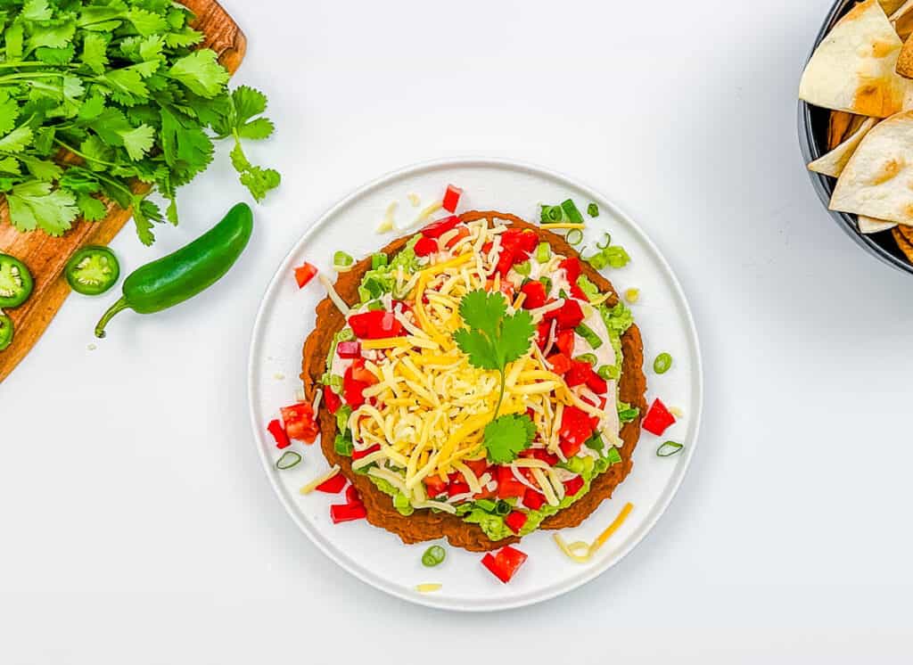 7 layer Mexican bean dip served on a white plate.