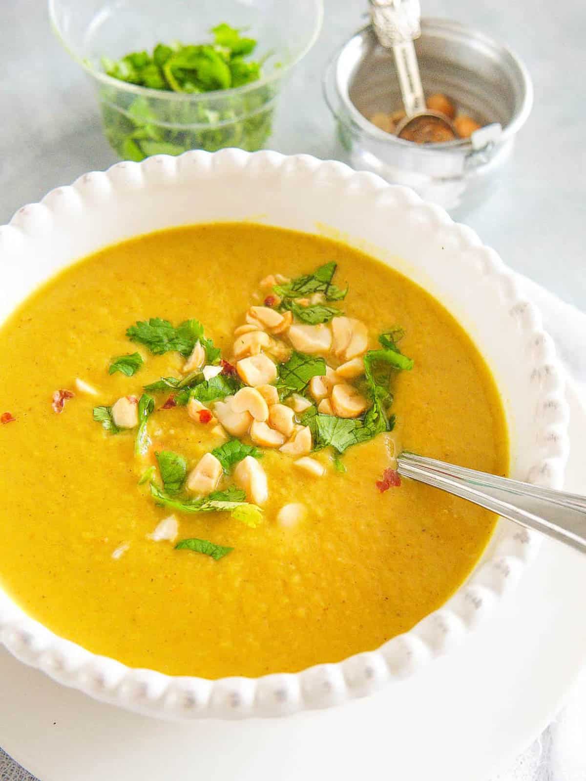 A side show of a white bowl of curried cauliflower soup with nuts and herbs.