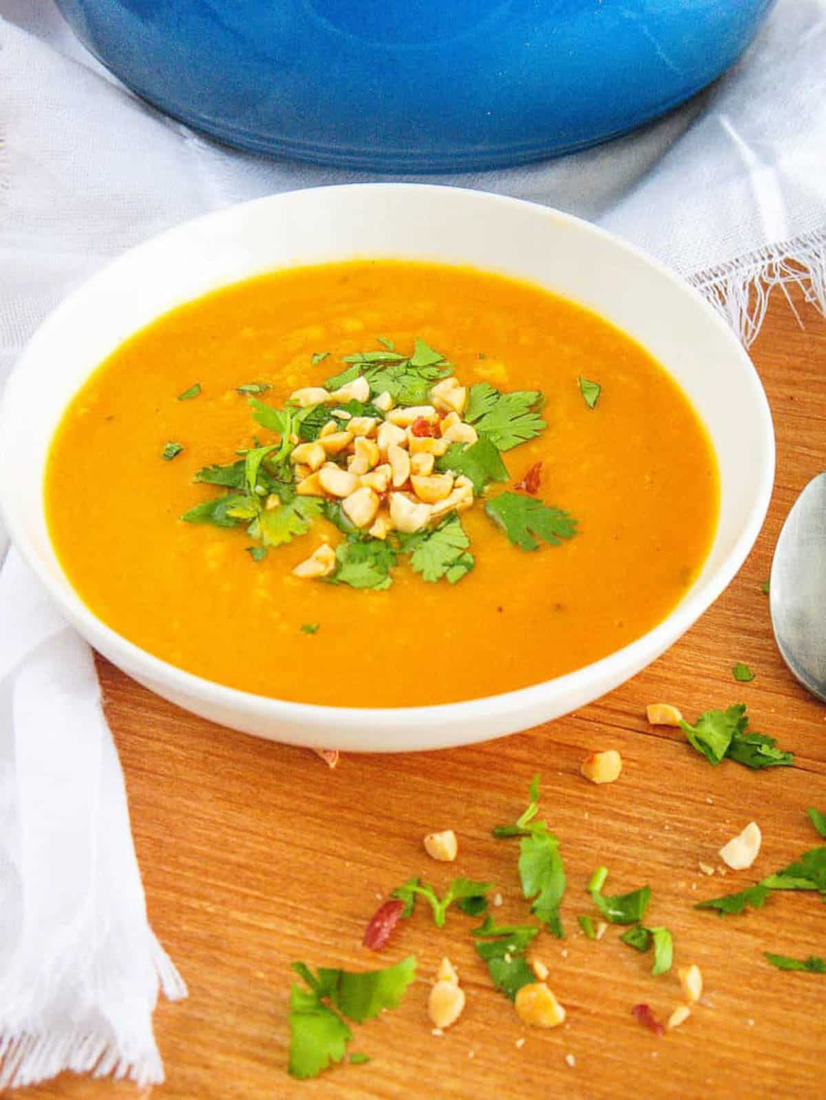 A closeup side shot of a white bowl of curried sweet potato soup with herbs and nuts.