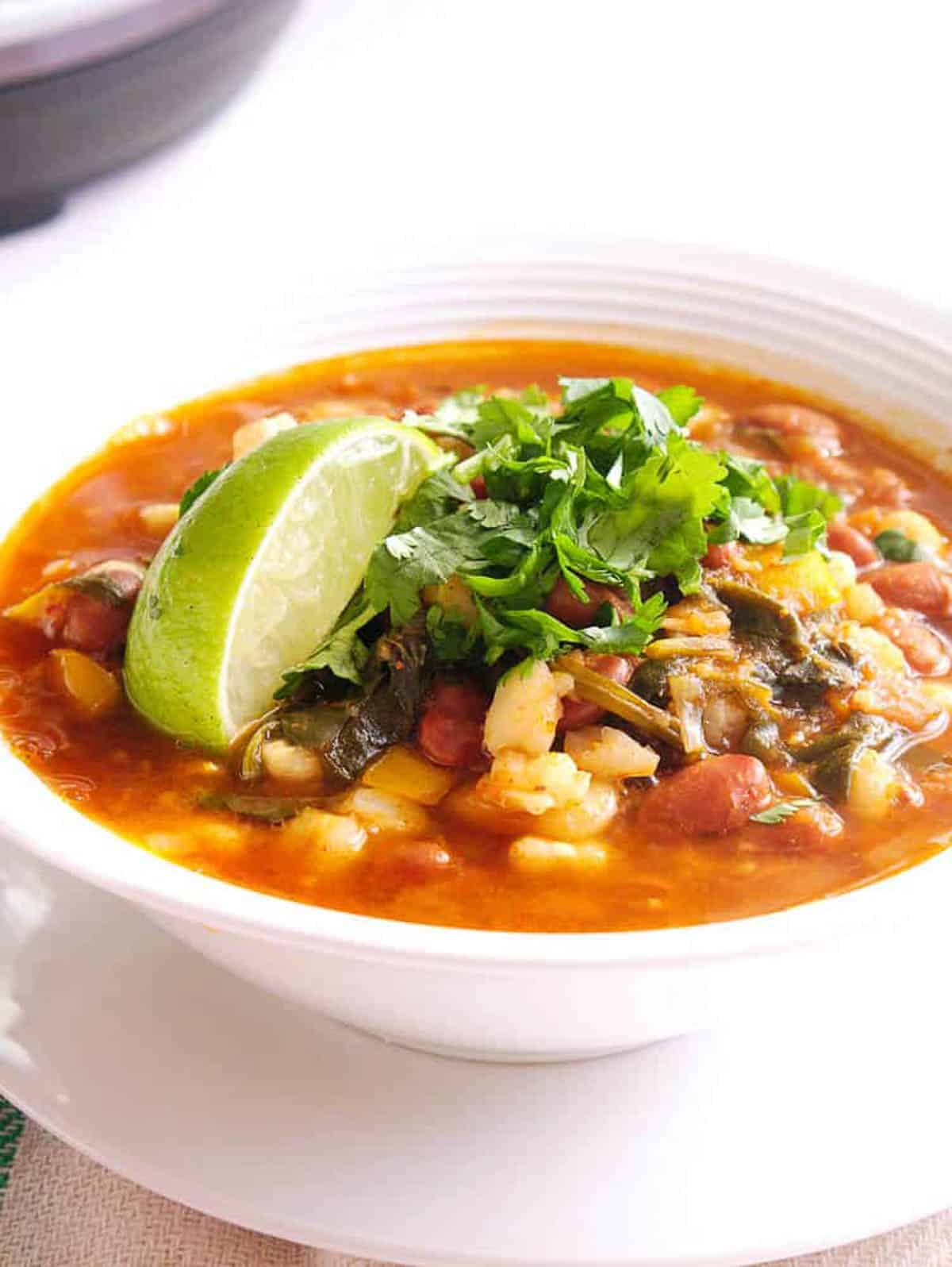 Closeup side s،t of a white bowl of vegan pinto bean pozole.