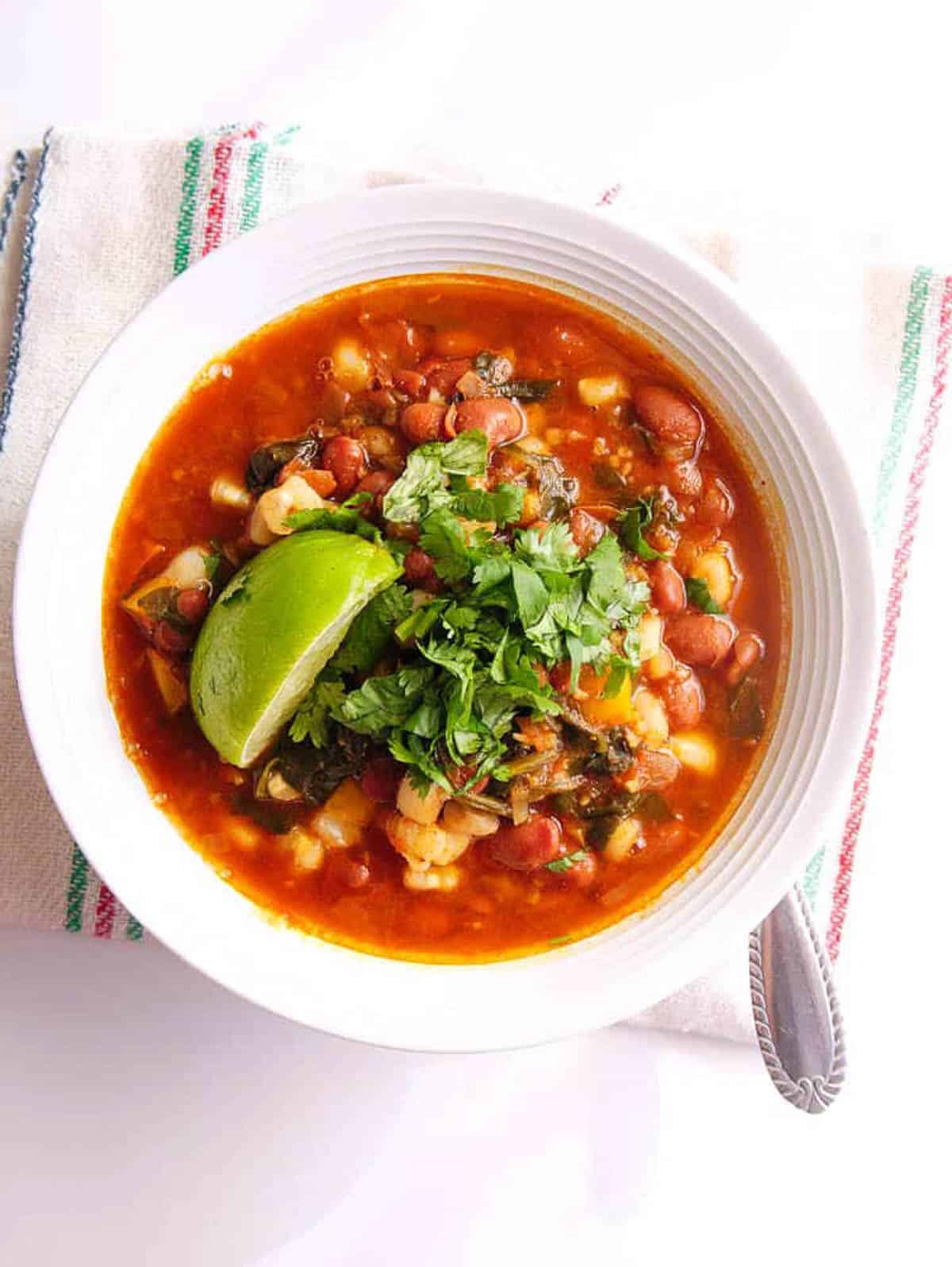 Overhead shot of a white bowl of pinto bean pozole with a napkin.