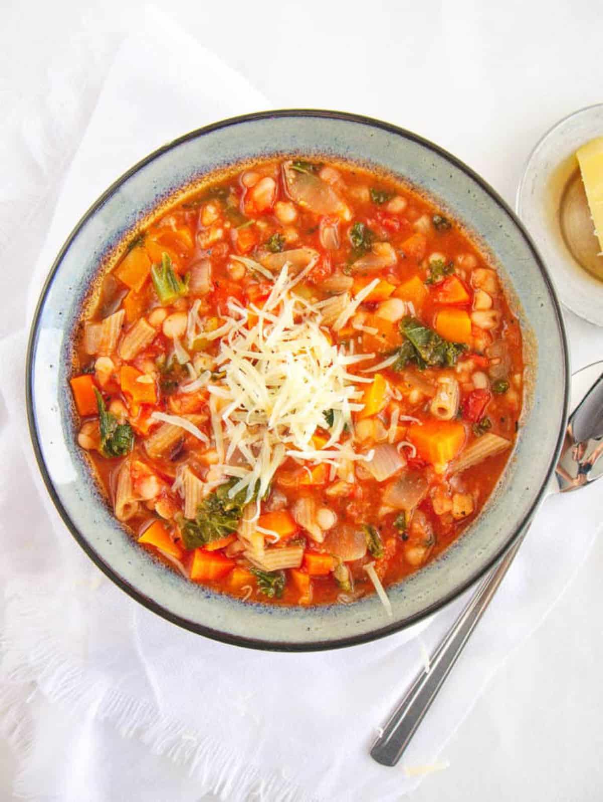 Overhead shot of a teal bowl of tuscan white bean soup with a spoon.