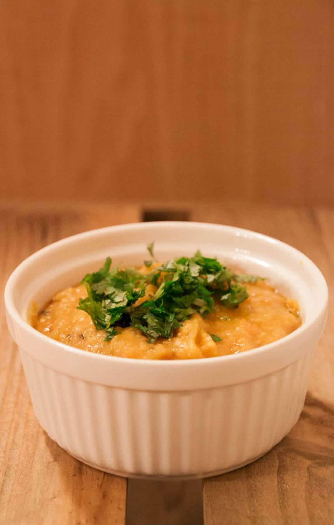 Side shot of a small dish of instant pot yellow dal with herbs.