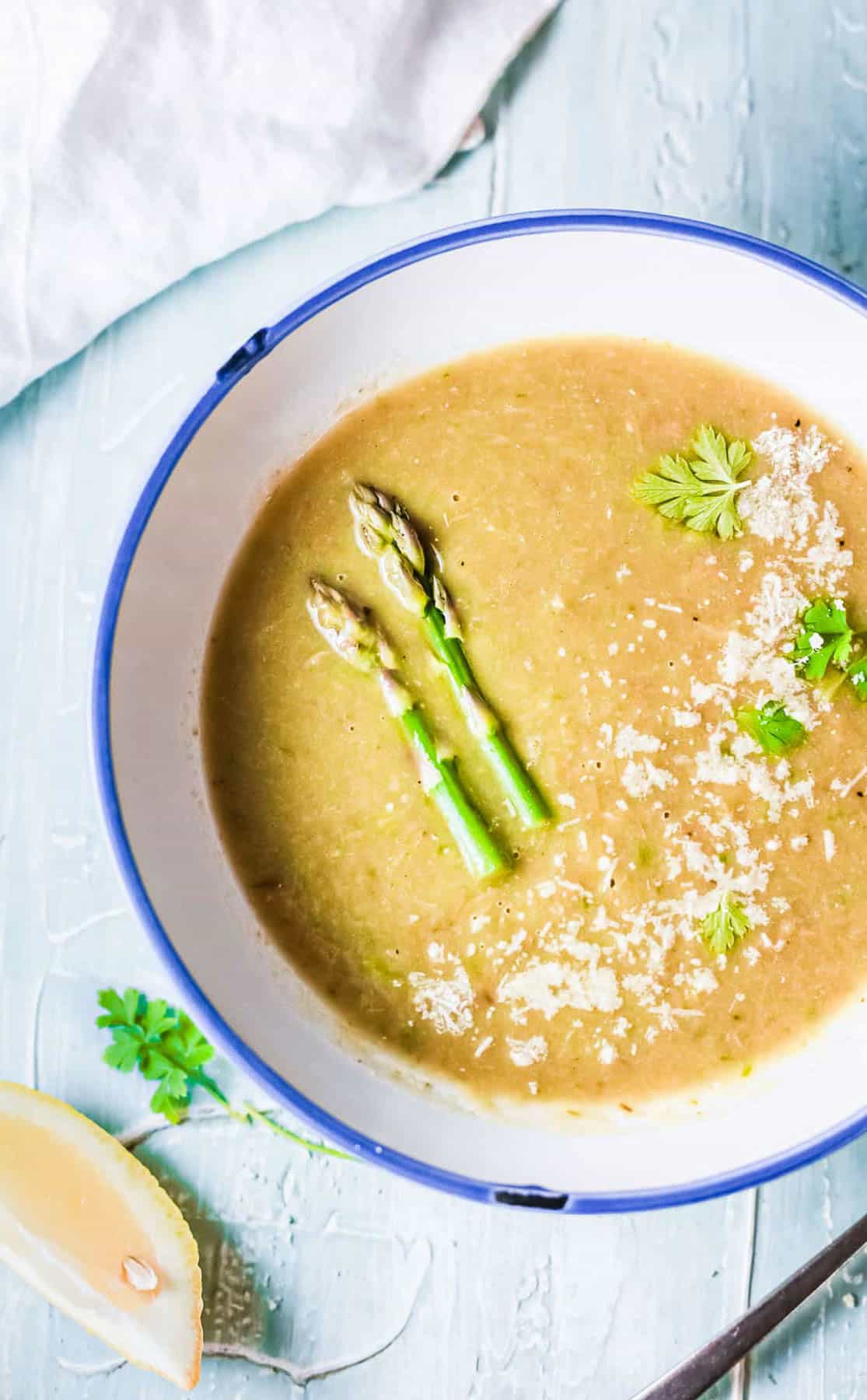 Overhead shot of a bowl of Instant pot asparagus soup with asparagus spears and herbs.