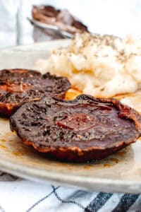 Portobello mushroom steaks paired with mashed potatoes and asparagus served on a white plate.