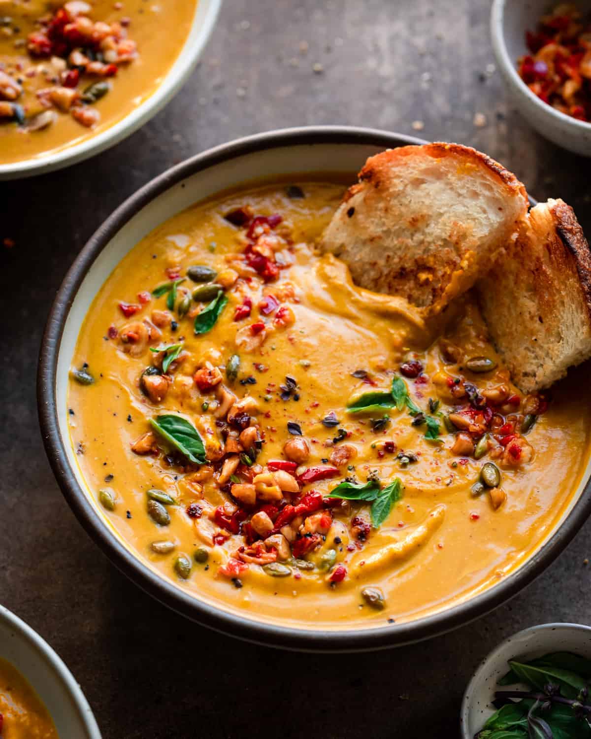 Up-closed angled shot of a bowl of thai pumpkin soup with seeds, nuts, and herbs.