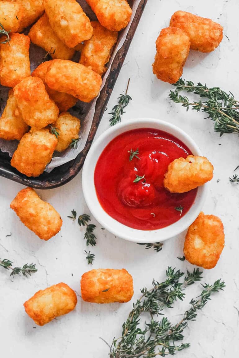 Air fryer frozen tater tots served with ketchup on a white countertop.