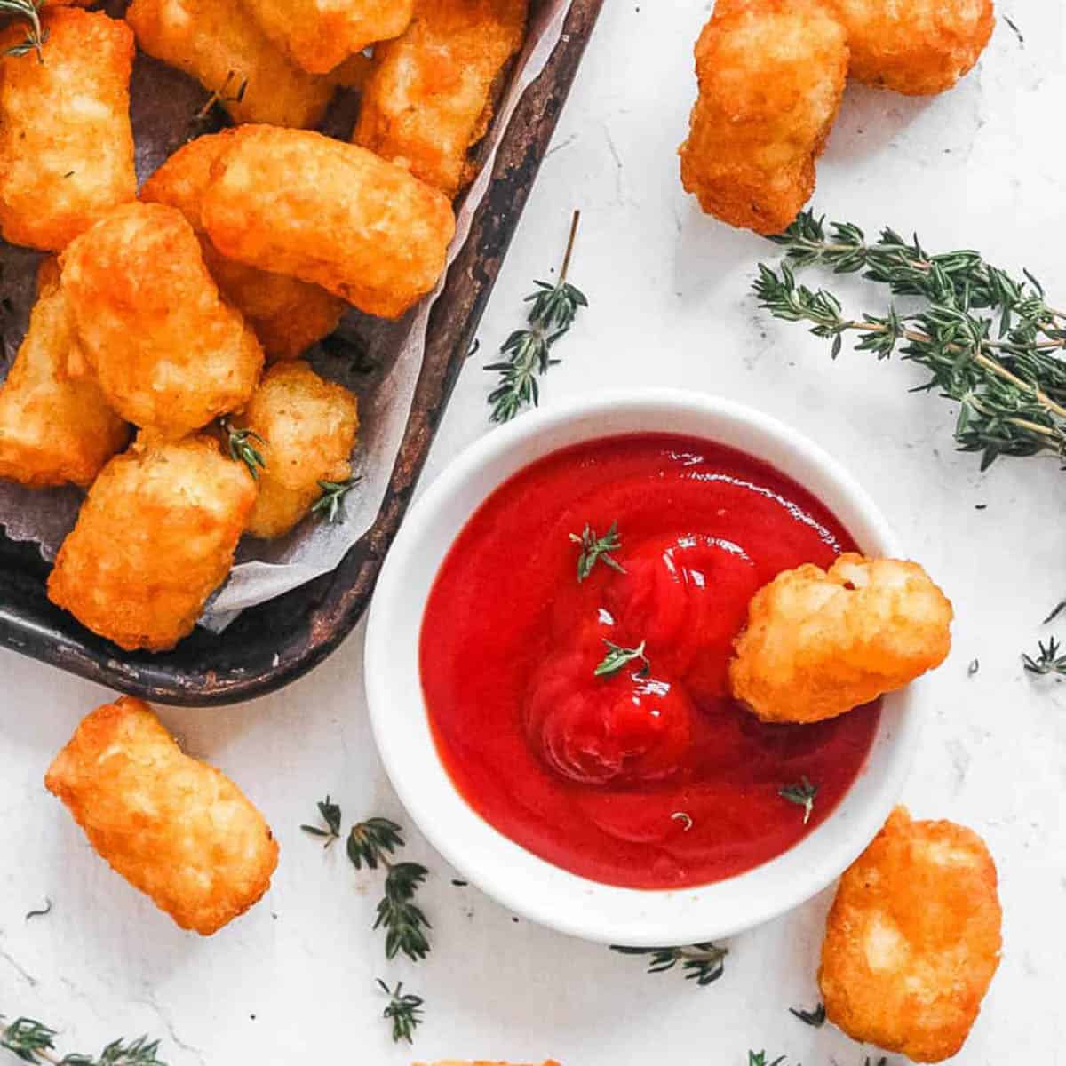 Air fryer tater tots served with ketchup on a white countertop.