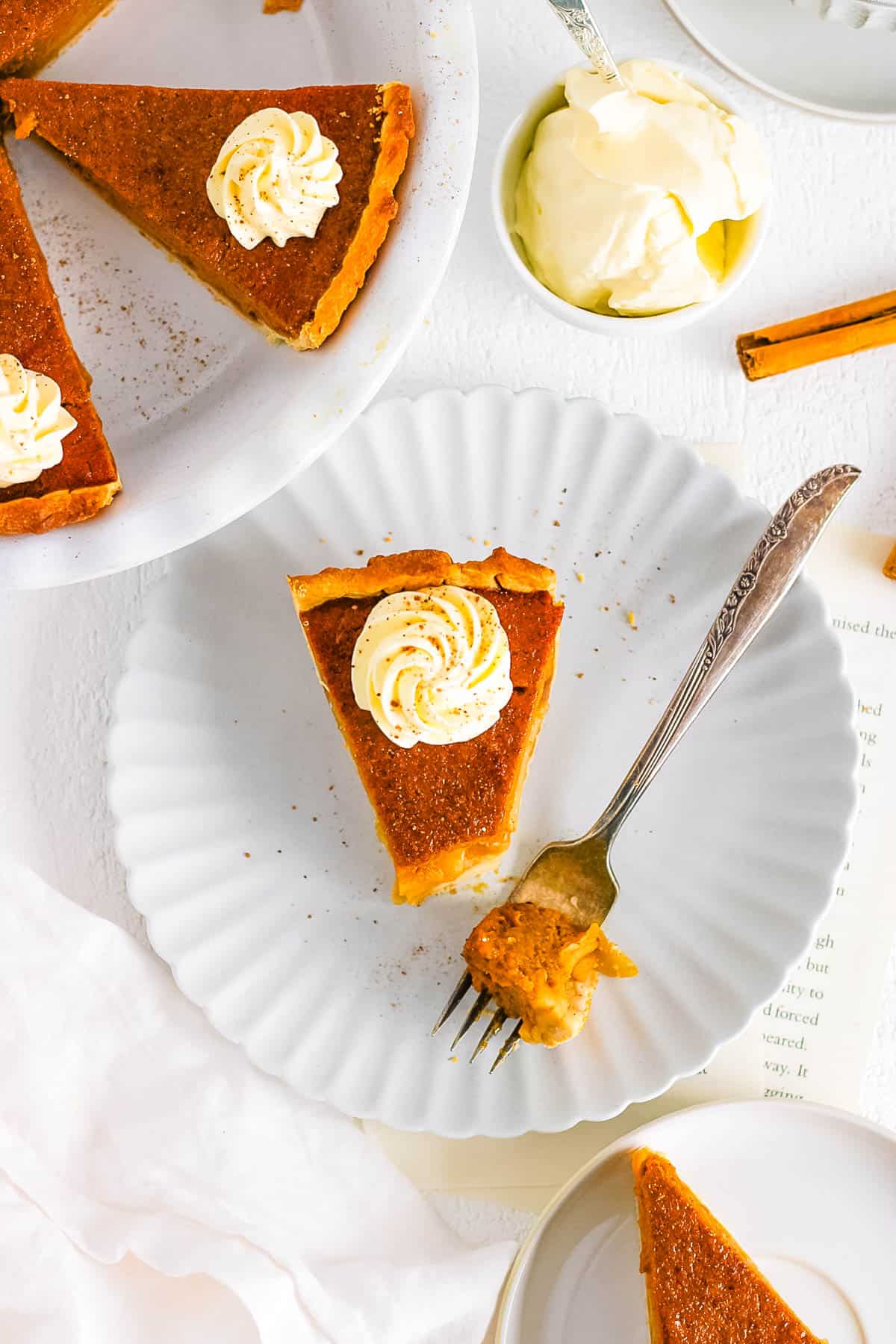 Slice of pumpkin apple pie on a white plate, topped with whipped cream, with a bite cut out with a fork.